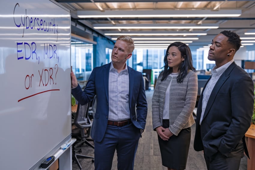 Cybersecurity professionals discuss 'Cybersecurity: EDR, MDR, or XDR?' written on a whiteboard in an office