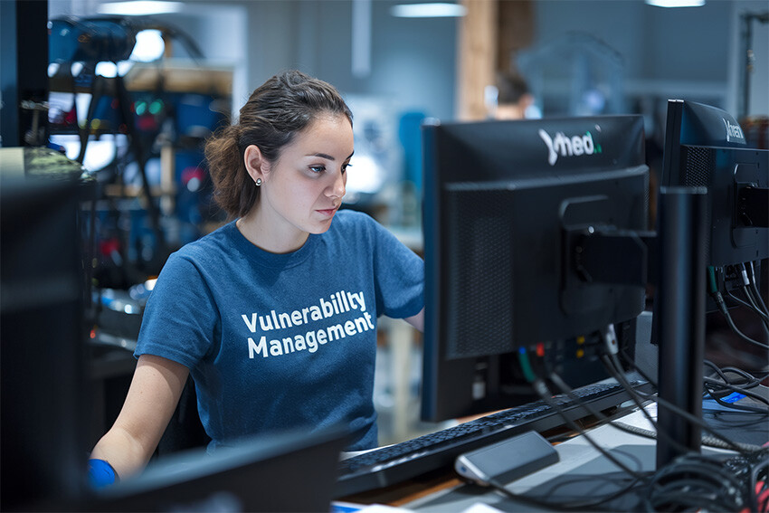 A woman cybersecurity engineer wearing a "Vulnerability Management" tshirt and focusing on her work intensely.